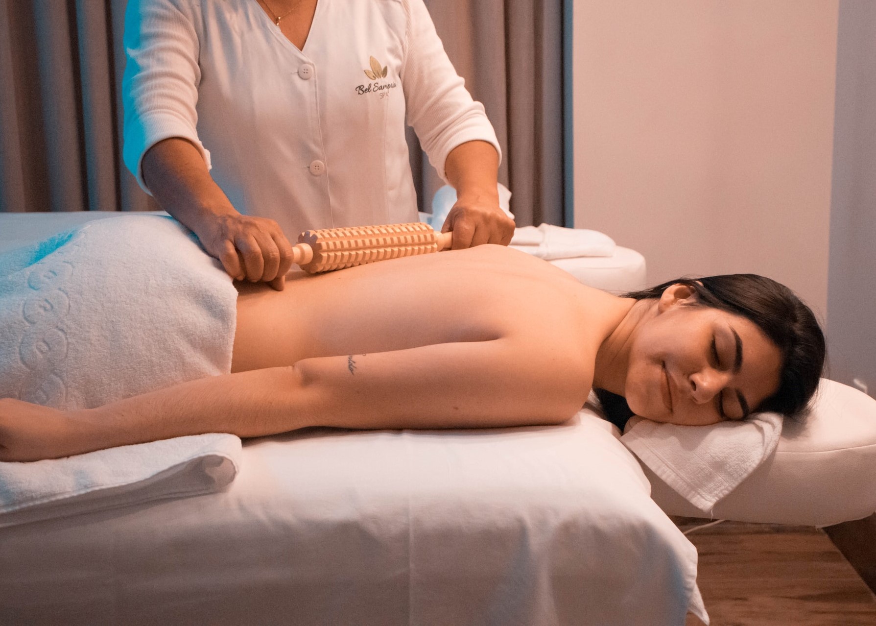 Mulher passando um rolo de bambu sobre as costas de outra mulher