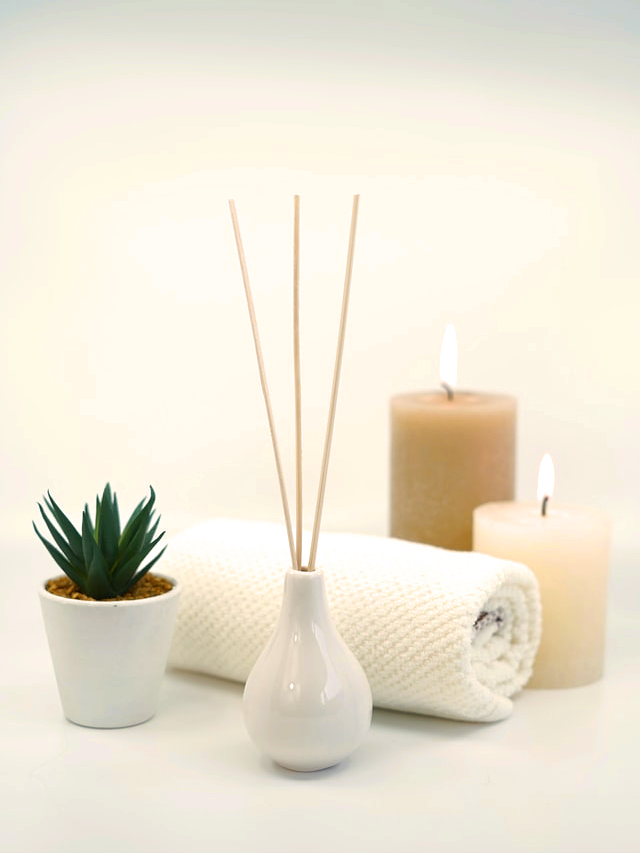 Imagem com difusor de aroma, velas, uma toalha branca e um vasinho de suculenta.